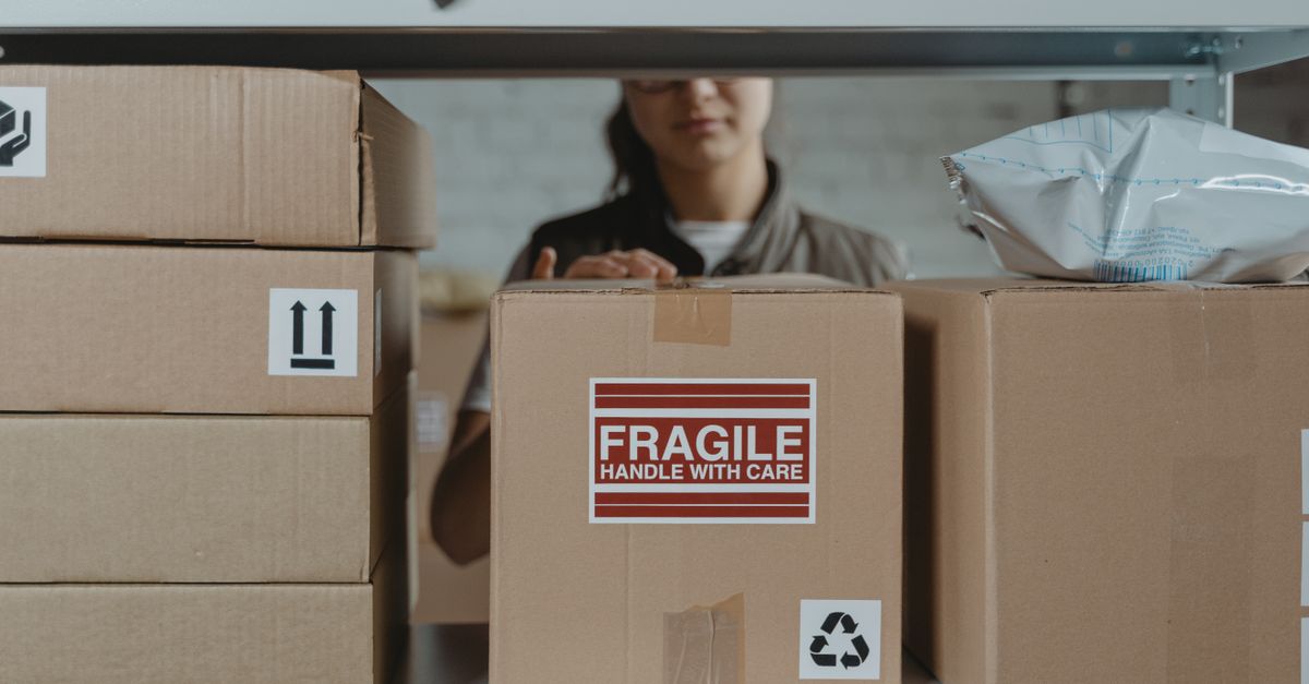 A person organizing fragile cardboard boxes in a warehouse setting.