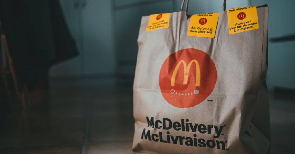 Beige package with bright yellow stickers and fast food on floor of apartment on blurred background
