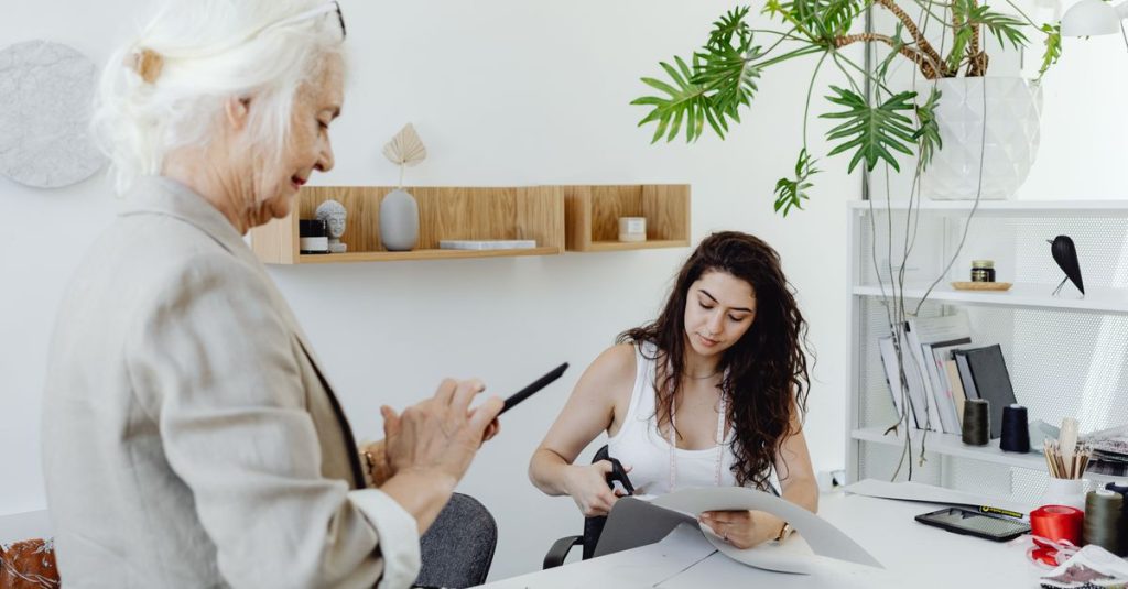 Two women collaborating in a modern design studio with fabrics and office decor.