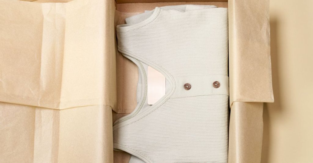 Minimalist packaging showcases a ribbed beige garment neatly folded inside a cardboard box.
