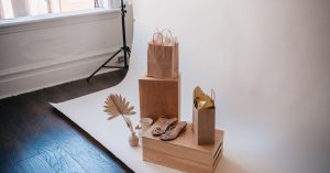 Stylish still life featuring shopping bags, sandals, and decor on a wooden box setup.