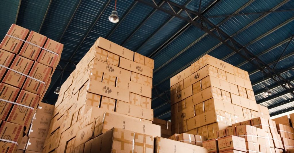 High stacks of cardboard boxes organized in a warehouse with a blue metal ceiling.