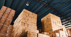 High stacks of cardboard boxes organized in a warehouse with a blue metal ceiling.
