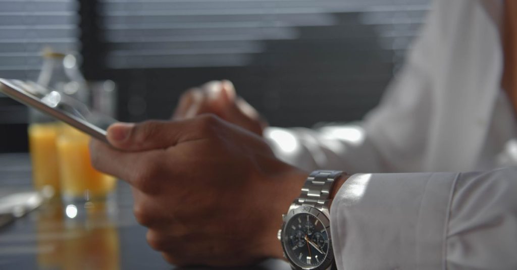 A man wearing a wristwatch holding a tablet in a softly lit room. Morning ambiance.