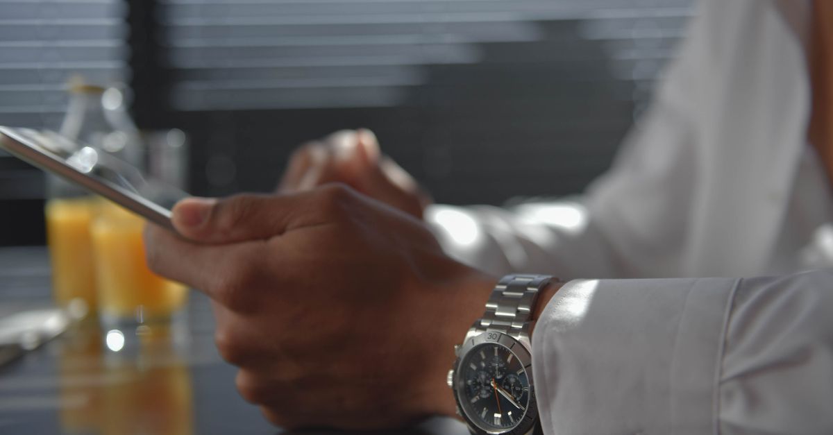 A man wearing a wristwatch holding a tablet in a softly lit room. Morning ambiance.