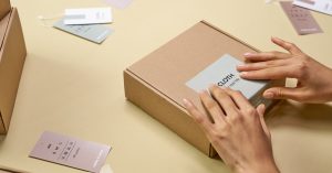 Hands carefully packing a cardboard box with multiple tags around, emphasizing sustainable packaging.