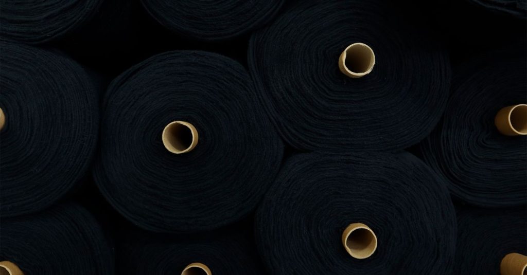 Circular rolls of black fabric stacked closely, showcasing textiles in an industrial setting.
