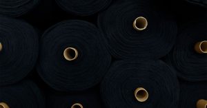 Circular rolls of black fabric stacked closely, showcasing textiles in an industrial setting.