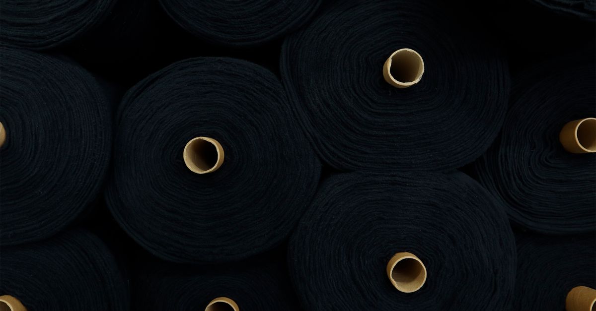 Circular rolls of black fabric stacked closely, showcasing textiles in an industrial setting.