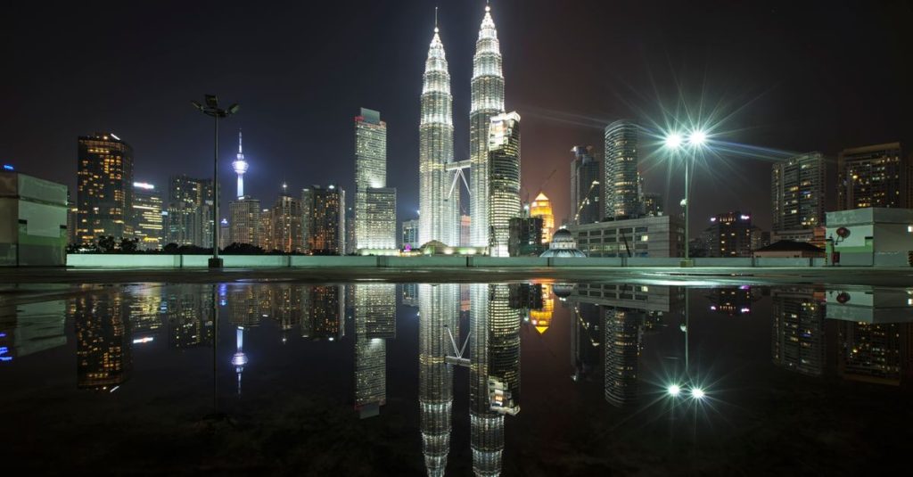 Beautiful view of Kuala Lumpur's skyline featuring the iconic Petronas Towers at night with city lights and reflections.