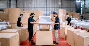 Men in a warehouse wearing masks, assembling and packing furniture into boxes with efficiency.