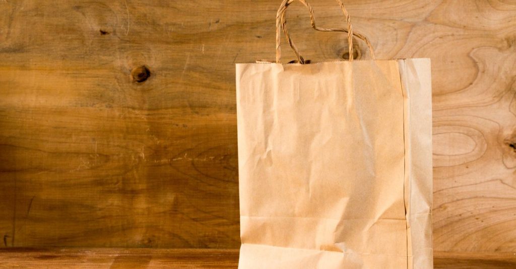 Close-up of a brown paper bag with handles on a wooden surface, offering warm earthy tones.