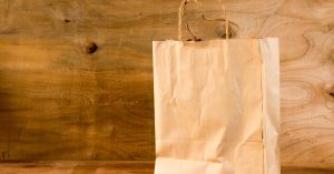 Close-up of a brown paper bag with handles on a wooden surface, offering warm earthy tones.